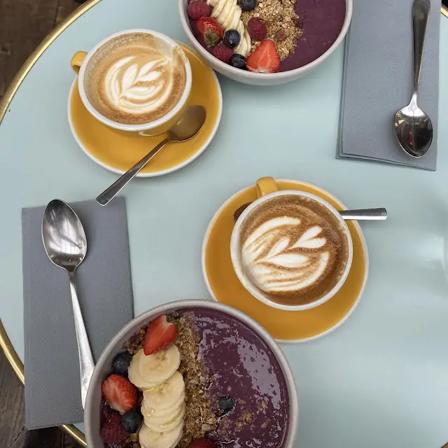 Deux açaï bowls aux fruits rouges et deux lattes sur une table menthe